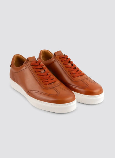 Pair of brown leather sneakers with white soles and brown laces on a light background.  
