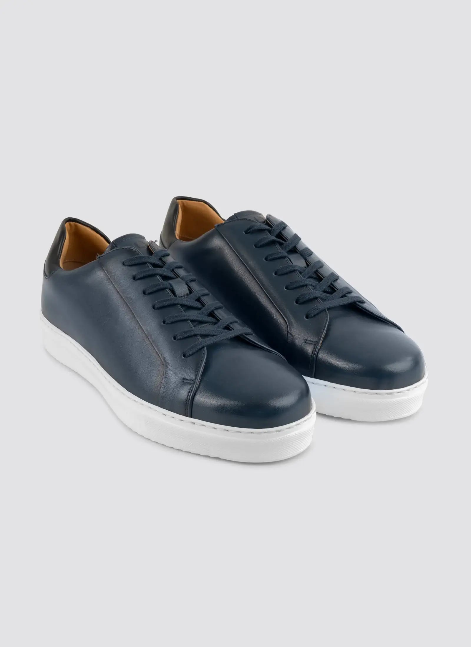 Pair of navy blue leather sneakers with white soles for men on gray background 