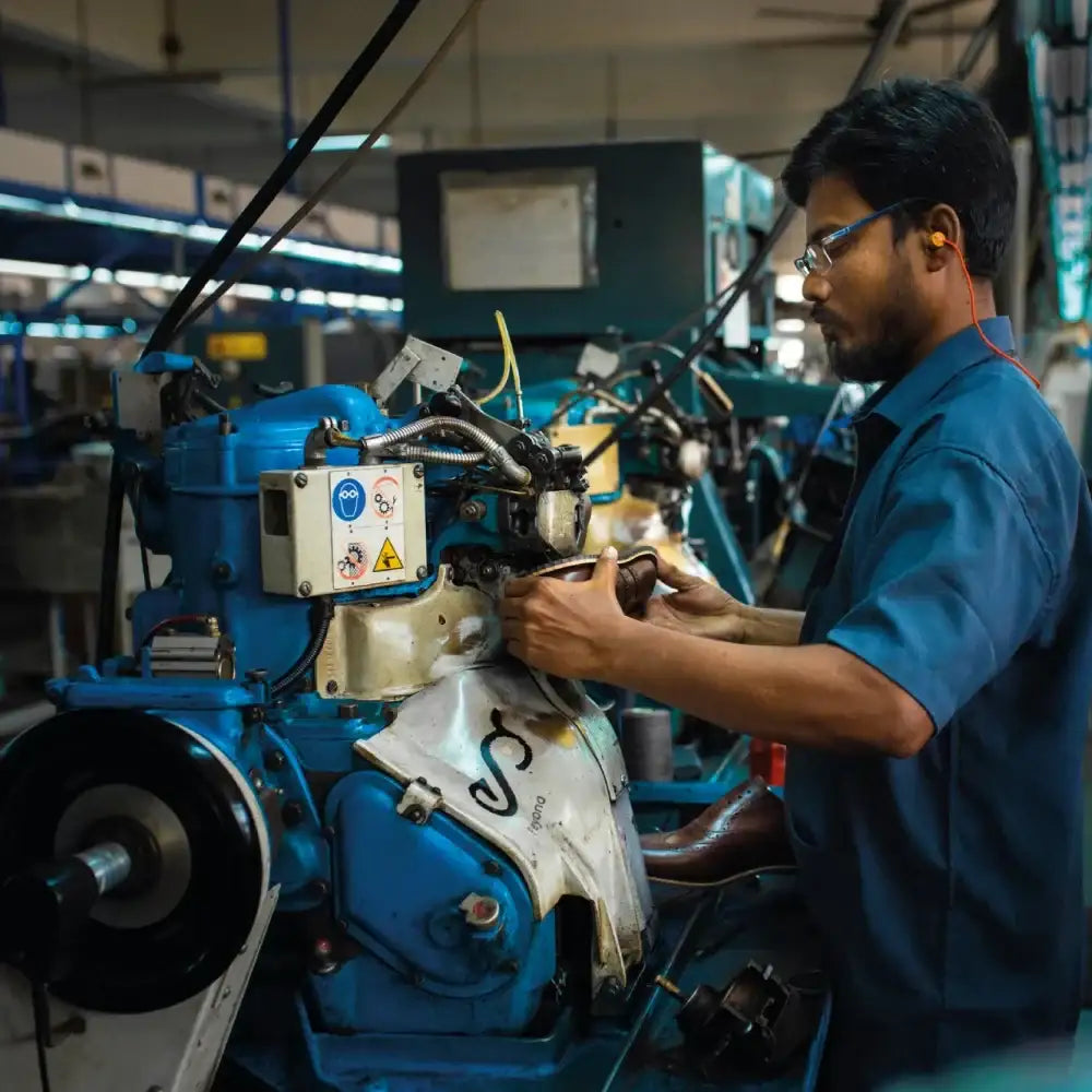 Craftsman shaping leather shoe using industrial shoe making machine in a factory
